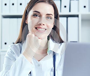 Attractive female doctor working on her laptop in her office. Happy doctor waiting for patient.