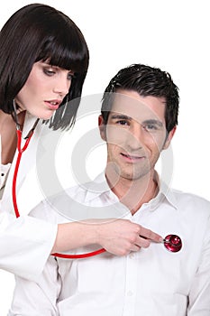 Attractive female doctorlistening to her male patient's heartbeat