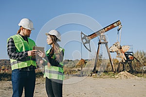 Attractive female engineer and foreman discussing about work schedule near an oil pumping unit. Work and engineering