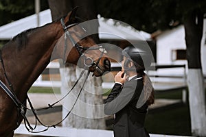 Attractive female equestrian in riding helmet looking at horse in horse club