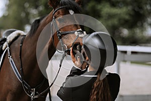 Attractive female equestrian in riding helmet looking at horse in horse club