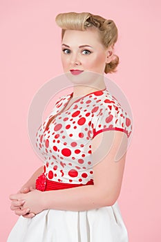 Attractive female feeling confidence holding hands and evaluating looking at camera. Blonde woman in white red spot dress
