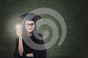 Attractive female graduate holding lit bulb in class