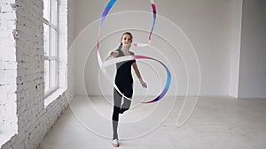 Attractive female gymnast dancing with ribbon in gymnastics school at white background and look at the camera. Rhythmic