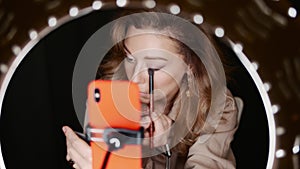 Attractive female makeup artist applies eyeshadow sitting in front of ring light