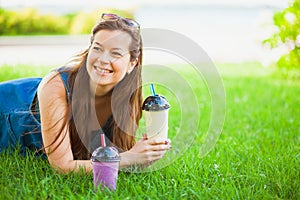 Attractive female model lie on grass field and drink fresh smoothie
