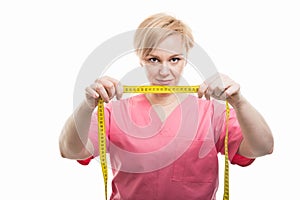 Attractive female nurse wearing pink scrubs holding measuring ta