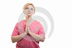 Attractive female nurse wearing pink scrubs making prayer gesture