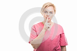 Attractive female nurse wearing pink scrubs making silent gesture