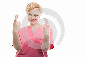 Attractive female nurse wearing pink scrubs showing double fingers crossed