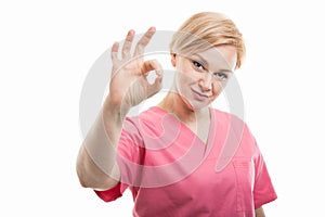 Attractive female nurse wearing pink scrubs showing ok gesture