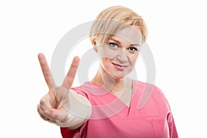 Attractive female nurse wearing pink scrubs showing peace gesture