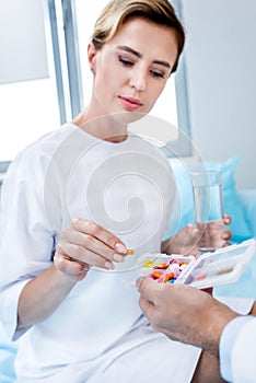 attractive female patient with glass of water taking pills from male doctor