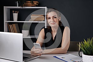 Attractive female person using phone in office sitting at the desk isolated.