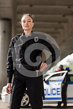 attractive female police officer in uniform looking at camera with blurred partner near car