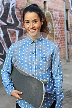 Attractive female skater holding her board in the skate alleyway smiling