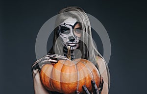 Attractive female with spooky makeup and pumpkin