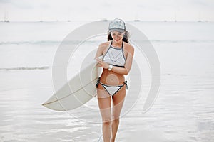 attractive female surfer in bikini with surfboard walking on beach