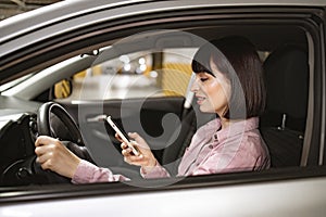 Attractive female typing on phone inside vehicle on underground parking lot.