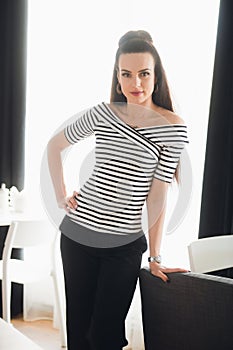 Attractive female wearing stylish striped shirt. Designer posing and looking at the camera in a cafe with huge windows