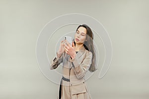 Attractive female worker in a beige suit uses a smartphone with a serious face on a beige background, wearing smart clothes