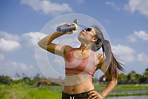 Attractive and fit Asian runner woman holding isotonic bottle drinking water after training and running series workout at outdoors