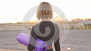 Attractive fit caucasian woman after workout on fresh air, woman holds mat in hands