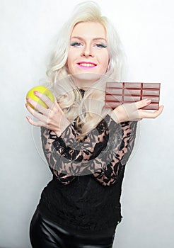 An attractive fit girl weighs her options of weather to eat chocolate or an apple. bad and good food.