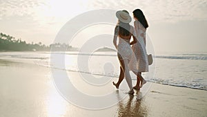 Attractive fit girls going at ocean shore at sunrise light. Happy carefree ladies enjoy summer vacation on sandy beach