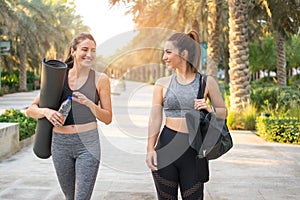 Attractive fit girls with sports equipment walking together in the park.