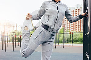 Attractive fit young woman in grey sport wear the doing warm up stretching before training on the street workout area. The healthy