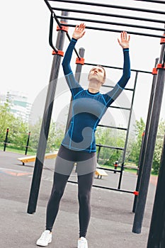 Attractive fit young woman in sport wear girl pulls up on the bar at street workout area. The healthy lifestyle in city