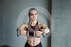 Attractive fit young woman in sport wear smiling girl trains with dumbbells at loft studio