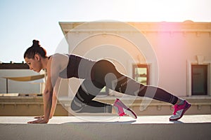 Attractive fit young woman wearing fitness clothes exercises on the edge of a wall on rooftop during sunset.