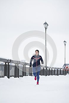Attractive fitness female model running at snow winter park, pink sneakers