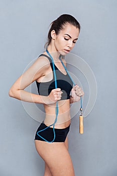 Attractive fitness girl holding skipping rope over grey background