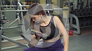 Attractive fitness girl practicing exercises with dumbbells in the gym. Young woman lifting weight in sport club.