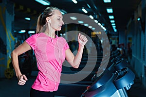 Attractive fitness girl running on machine treadmill. Pretty girl doing workout at modern fitness gym.