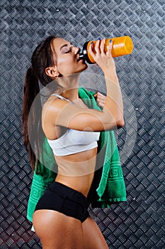 Attractive fitness woman with bottle and towel indoor portrait, drinking.