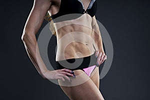 Attractive fitness woman on gray background in studio. Muscular abdomen close-up