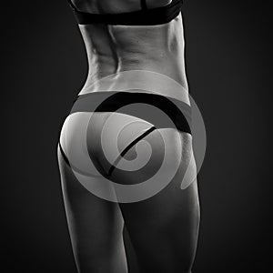Attractive fitness woman on gray background in studio. Muscular buttocks close-up
