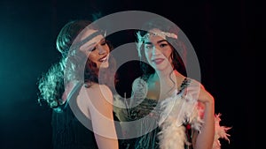 Attractive flappers women dressed in Roaring twenties time dancing on party in neon smoke room. retro fashion, vintage