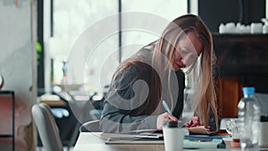 Attractive focused young 30s blonde entrepreneur business woman works with documents at modern light trendy office table
