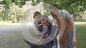 Four students laugh at what they see on laptop on campus