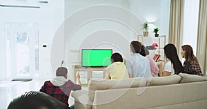 Attractive friends in a big living room watching on a green screen TV a football match they support their best football