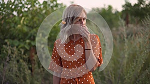 Attractive fun hippie blonde woman eating an apple in a field at sunset, having good time outdoors