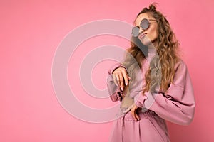 Attractive funny amusing young blonde woman wearing everyday stylish clothes and modern sunglasses isolated on colorful