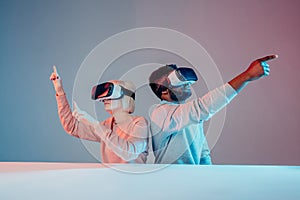 Attractive funny man and woman pointing at somewhere while playing VR game