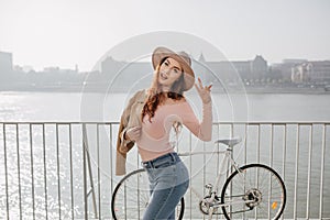 Attractive ginger girl wears pink shirt enjoying sunny day near sea. Outdoor photo of gorgeous red-haired lady in jeans