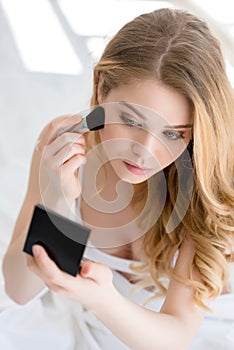 attractive girl applying blush with brush and looking photo